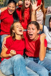 Group of enthusiastic women wearing red shirts and face paint, celebrating with open mouths and