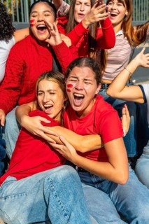 Group of excited young women wearing red, cheering loudly with face paint on their cheeks,