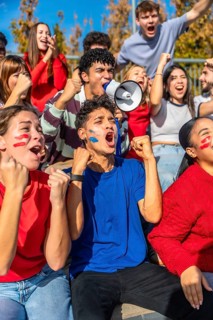 Diverse group of young sports fans cheering passionately in stadium stands, face paint and