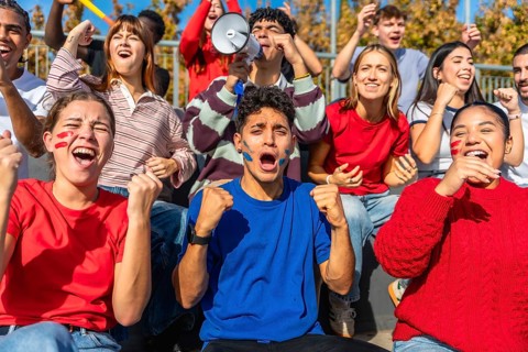 Excited sports fans yelling and cheering with painted faces, pumping fists, and using a megaphone