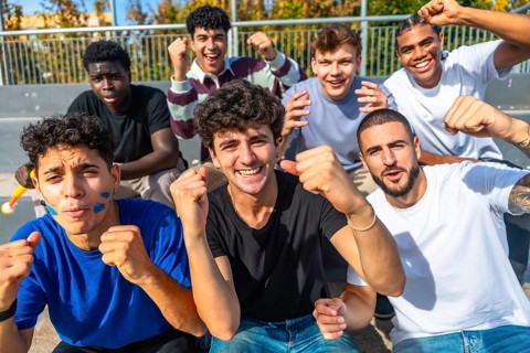 Enthusiastic young diverse male friends sitting on grandstand steps watching a sports event,