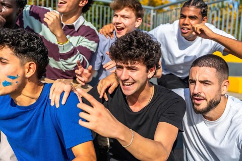 Diverse young male friends are excitedly cheering on their team from stadium stands, showing