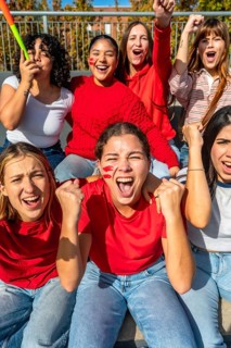 Group of excited young women with face paint and red clothing cheering passionately during a