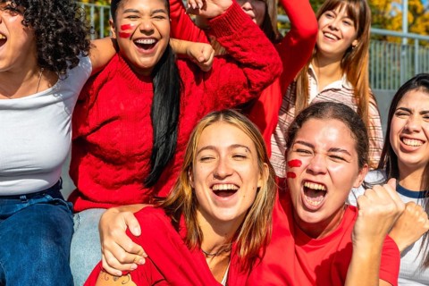 Group of enthusiastic young women friends celebrating together at a stadium, wearing red clothing