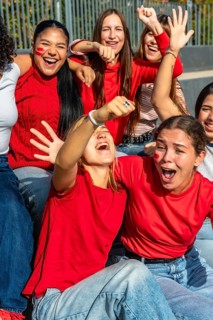 Diverse young women in red t shirts with face paint cheering and celebrating together at a stadium,