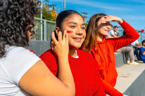 Young happy female friends enjoying a game at an outdoor stadium, painting faces and cheering for