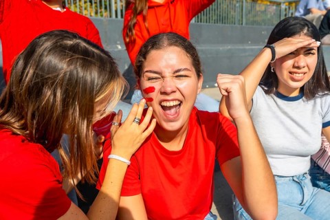 Young female friends in red team colors and face paint are thrillingly watching a sports event,