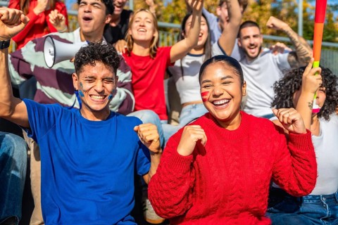 Diverse group of young sports fans cheering with painted faces and team colors in a stadium,