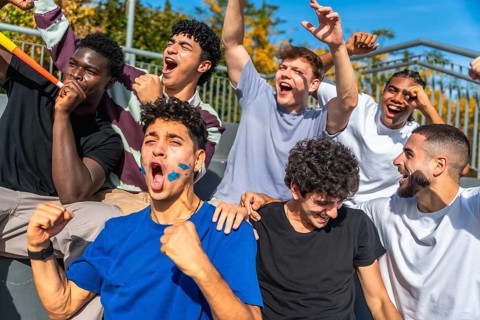 Diverse group of young men with painted faces and horns celebrating loudly, showing excitement and