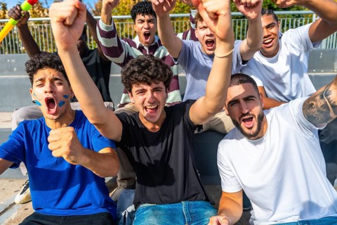 Excited multiethnic male friends cheering and raising fists in outdoor stadium, standing together