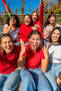Group of excited young women friends watching a sport game, wearing red shirts and face paint,