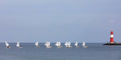 Sailing course with Optimist class sailboats, a sailing dinghy and the pier fire in Warnemünde,