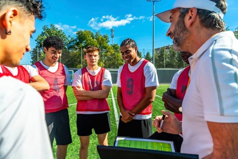 Soccer coach discussing game strategy and explaining tactics on a digital tablet with a group of