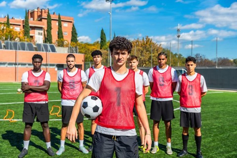 Diverse group of young male soccer players wearing red bibs and shorts, standing confidently on a