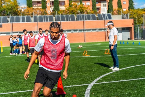 Young male soccer player in a red bib practices drills on green artificial turf with teammates