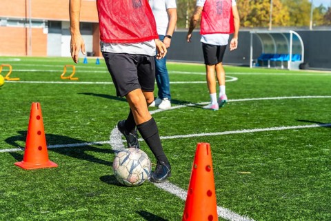 Football player practicing drills with ball and cones on artificial green turf, focused on