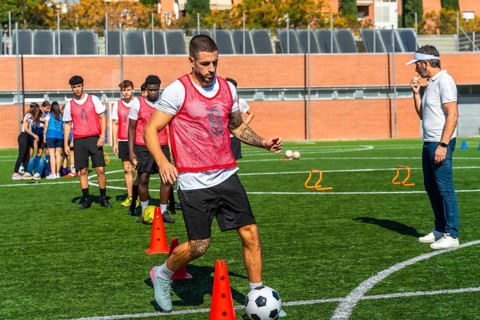 Soccer player in a red bib training on a green artificial turf field, dribbling a football around