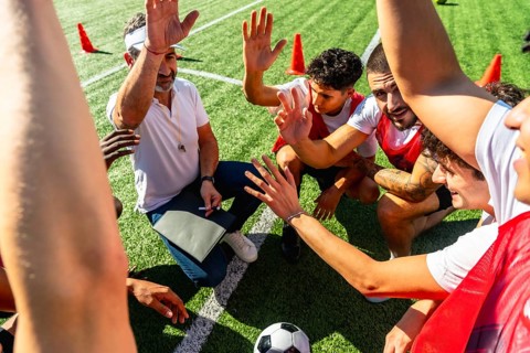 Soccer coach giving instructions and motivating his diverse team during a huddle on a green turf