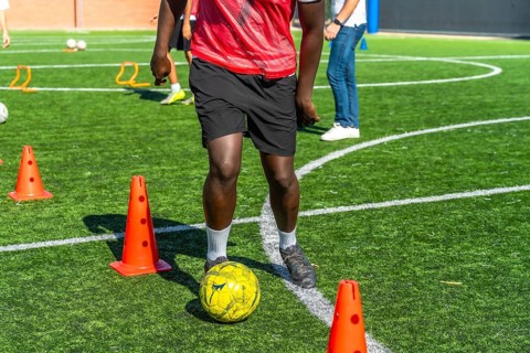 Young player actively training and practicing soccer drills, dribbling the ball around orange cones