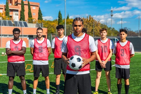 Young men from diverse backgrounds forming a soccer team, standing on a green artificial turf field