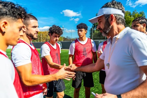 Soccer coach motivating and encouraging young male players with a handshake on a training field