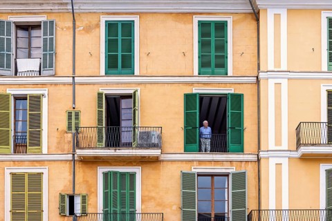 Senior citizen standing and looking out from open window in an old apartment building with