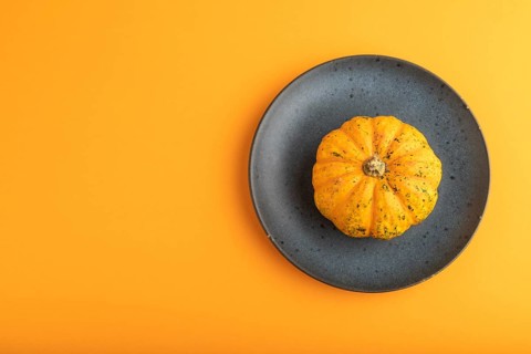 Orange Pumpkin on blue plate on orange pastel paper background. Top view, copy space, flat lay.