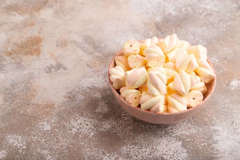 Orange and pink marshmallow in ceramic bowl on brown concrete background, side view, copy space,