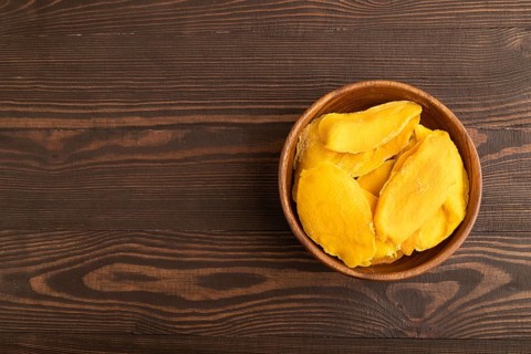 Dried Mango in wooden bowl on brown wooden background. Top view, copy space, flat lay. healthy