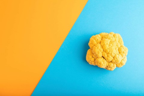 Yellow Cauliflower on blue and orange pastel paper background. Top view, flat lay, copy space.