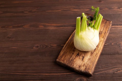 Fresh Fennel bulb on wooden cutting board on brown wooden background, side view, copy space,