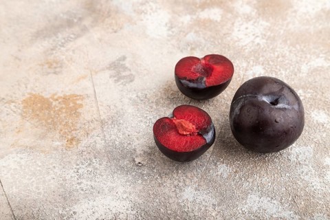 Purple Plum Cut in half on brown concrete background. Side view, copy space. healthy food,