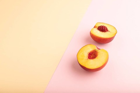 Peach Cut in half on orange and pink paper pastel background. Side view, copy space. healthy food,