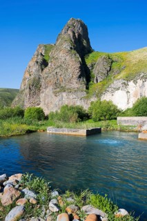 Clear water flows through a green landscape, framed by majestic, sunlit rocks, hot spring, Vorotan,
