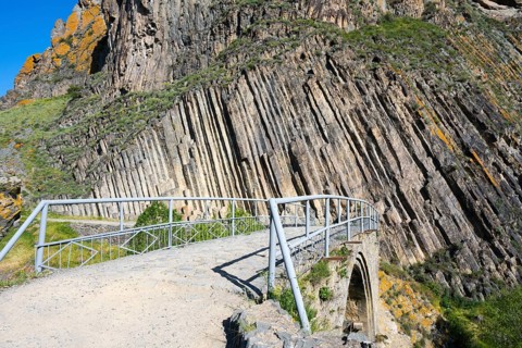 A narrow path with railing leads over a stone bridge, surrounded by unique vertical rock