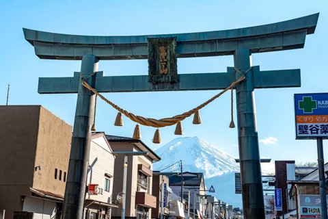 Large torii gate on above a street, street scene, in the back volcano Mt. Fuji, Fujiyoshida,