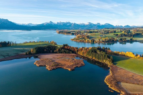 Wide landscape with calm lake and colorful trees against alpine backdrop, Illasbergsee, Forggensee,