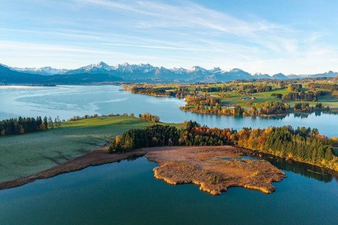 Landscape with clear lake surrounded by autumn forests and alpine scenery on the horizon,