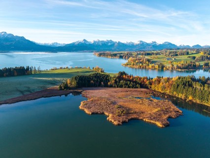 Clear lake, surrounded by autumn trees, with alpine peaks on the horizon under clear sky,
