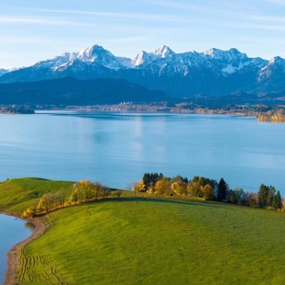 Green hills and trees on the shores of a quiet lake against the backdrop of majestic alpine