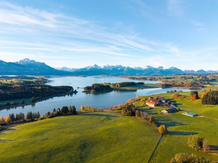 Green meadows and a farm on the shore of a lake with mountains in the background, Illasbergsee,
