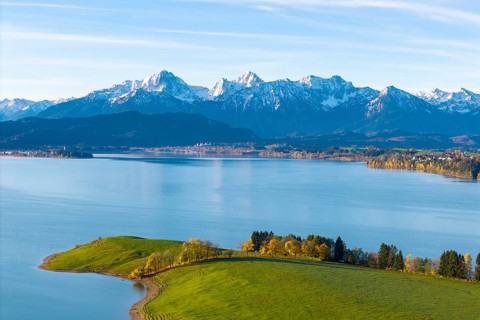 View over quiet lake and rolling hills to the chain of snow-capped alpine mountains in the
