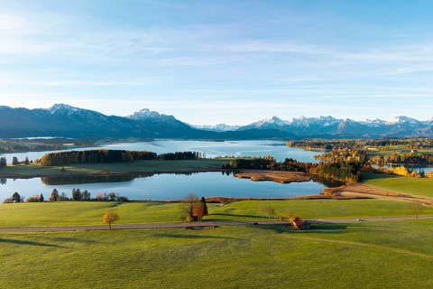 Extensive scene with lake and mountains, surrounded by green meadows and autumn colors,