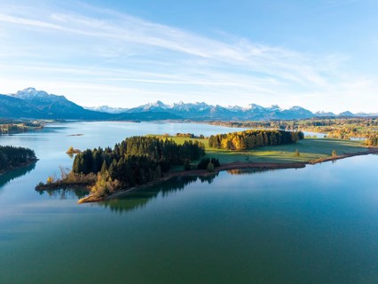 Tranquil landscape with a still lake and autumnal forests in front of an alpine panorama,