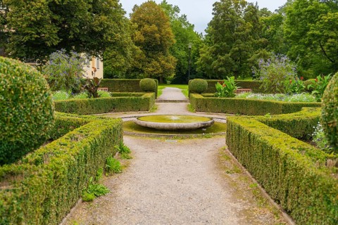 A symmetrical garden with well-kept hedges and a central path leads through the green area, ZFP