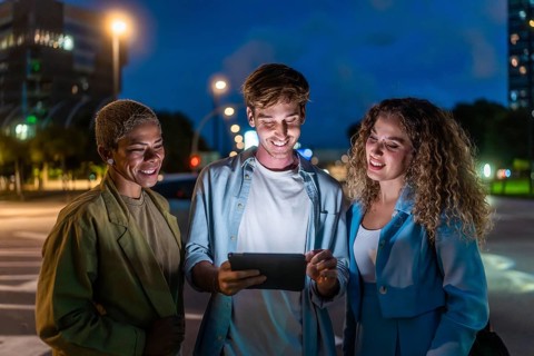 Three diverse friends, two women and one man, standing on a city street at night, smiling and