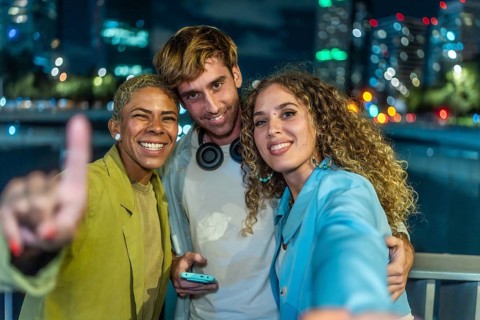 Three happy diverse friends are taking a selfie together, smiling at the camera and celebrating