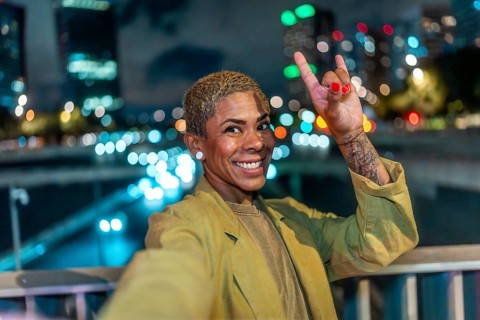 Happy woman with short blond hair and a tattoo making a rock and roll hand gesture, smiling at the