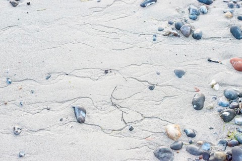 Pattern in sand with scattered stones on a quiet sandy beach, drainage channels, runoff water,
