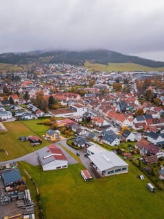 Small town with red roofs surrounded by fields and wooded hills under cloudy sky, Wehingen,